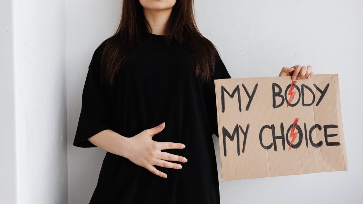 Woman holding 'My Body My Choice' sign, advocating for women's rights indoors.